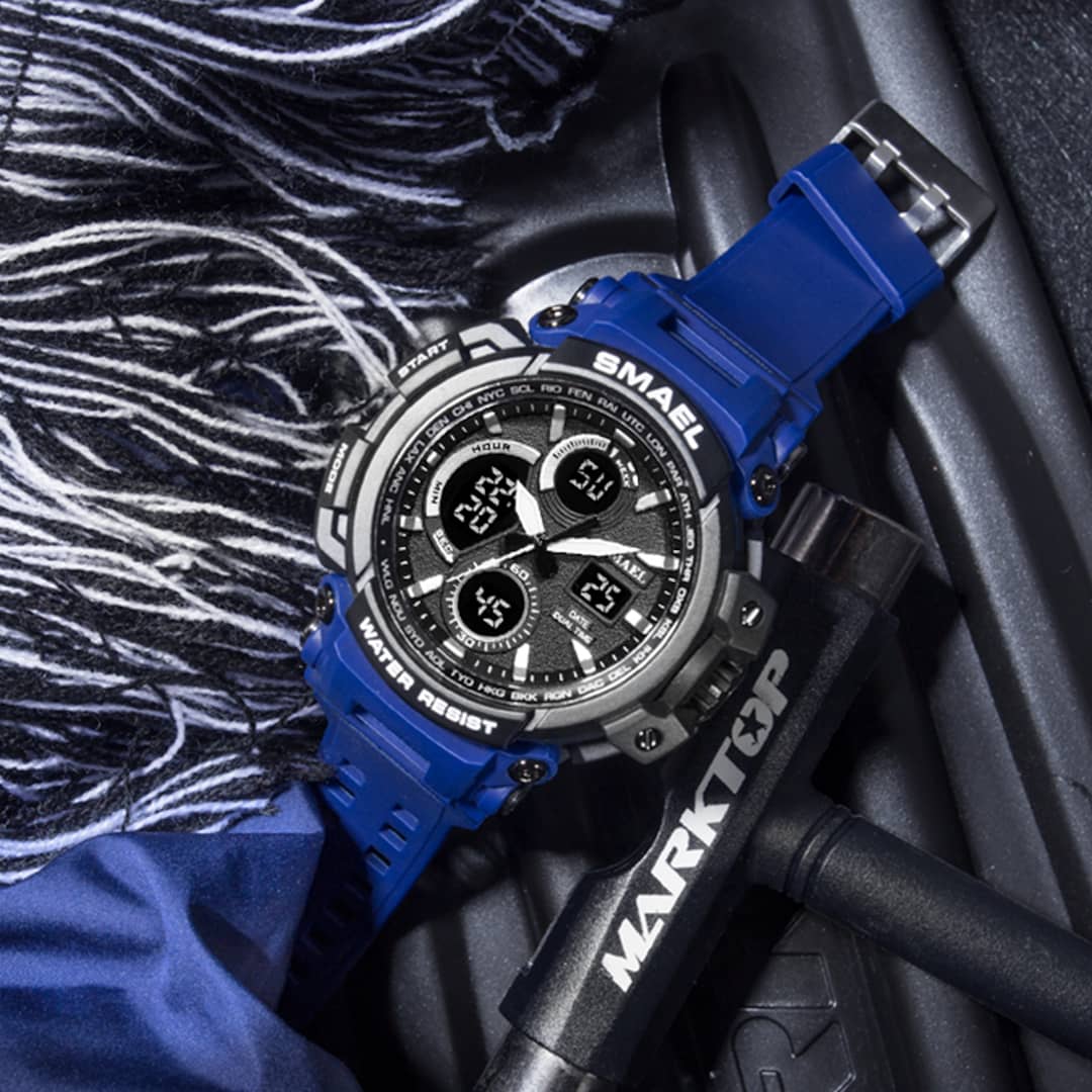 Muški ručni sat Smael S-shock MTGB1000 Blue s izdržljivim crno-plavim dizajnom, prikazan na sportskoj opremi.